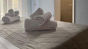 A neatly made bed with rolled white towels, a blue wall, and a door leading to a bathroom. - Hotel Eureka (Rimini)