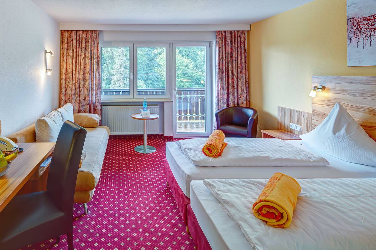 Une chambre d’hôtel avec deux lits, un bureau avec une chaise, une télévision et une fenêtre avec des rideaux.
