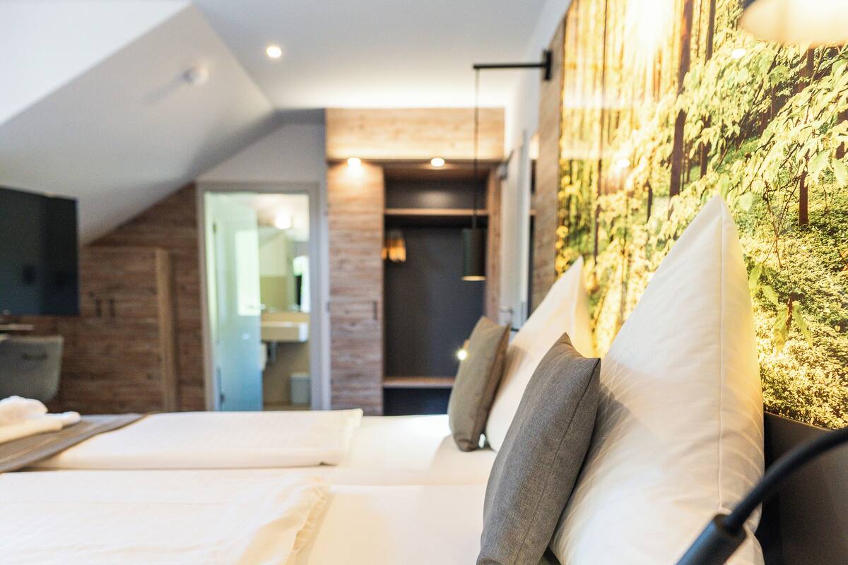 Une chambre d’hôtel moderne avec un grand lit, une tête de lit en bois et un téléviseur fixé au mur.