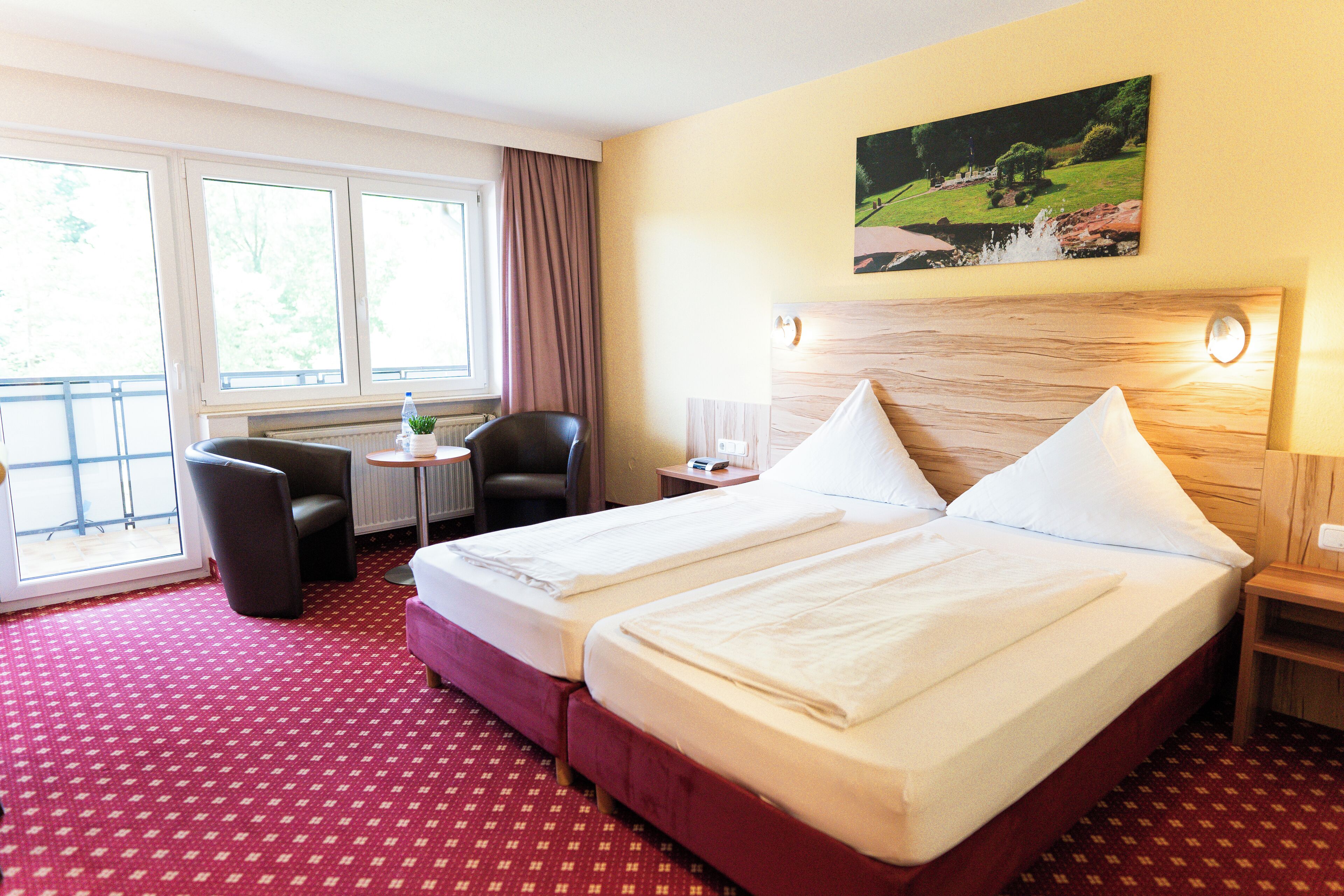 Ein Hotelzimmer mit zwei Betten, einem Sessel, einem kleinen Tisch und einem Fenster mit Vorhängen.