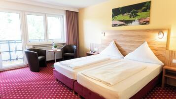 Ein Hotelzimmer mit zwei Betten, einem Sessel, einem kleinen Tisch und einem Fenster mit Vorhängen.