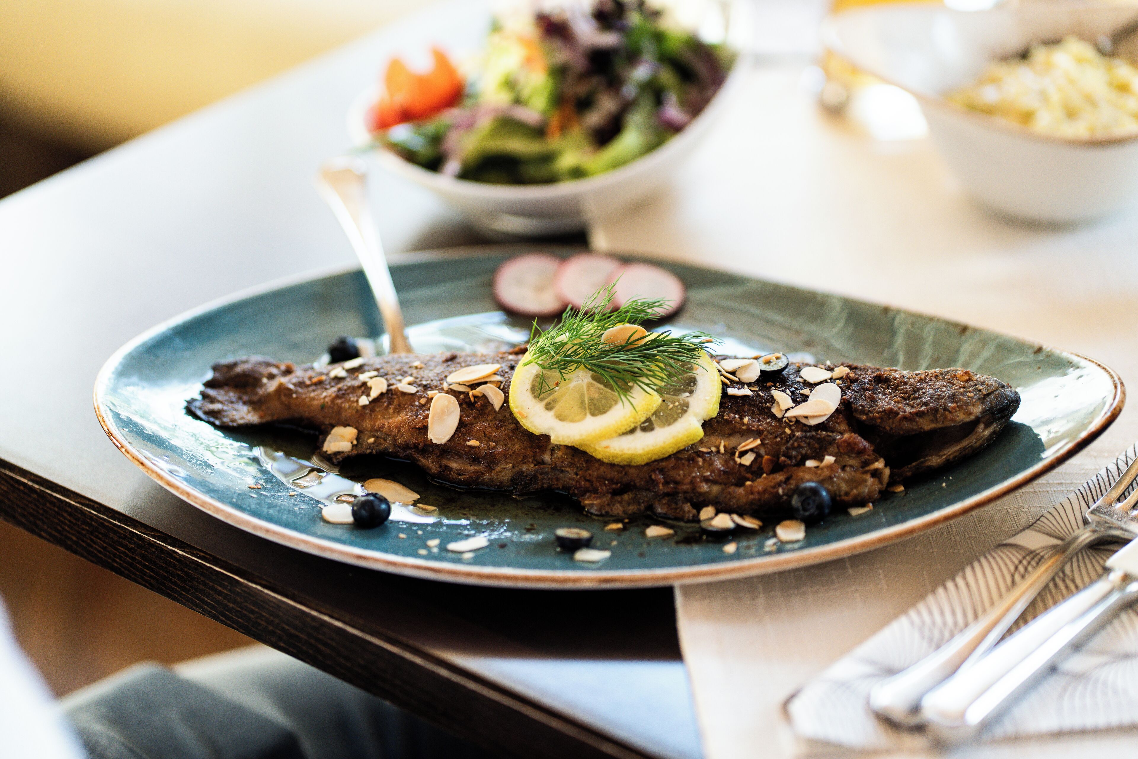 Une assiette de steak, garnie de tranches de citron et d’amandes, sur une assiette bleue.