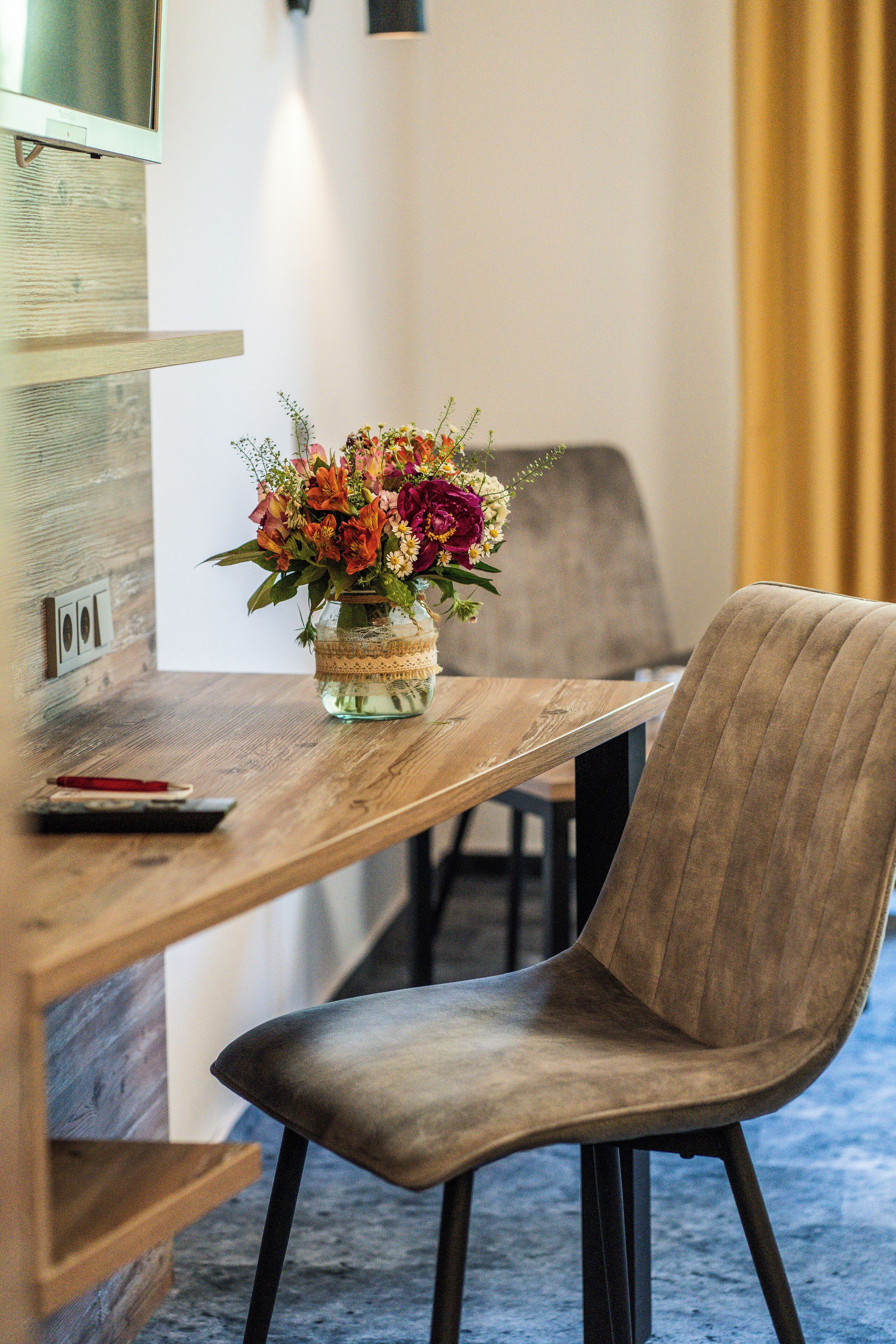 A wooden dining table with a vase of flowers, a remote control, and a chair.
