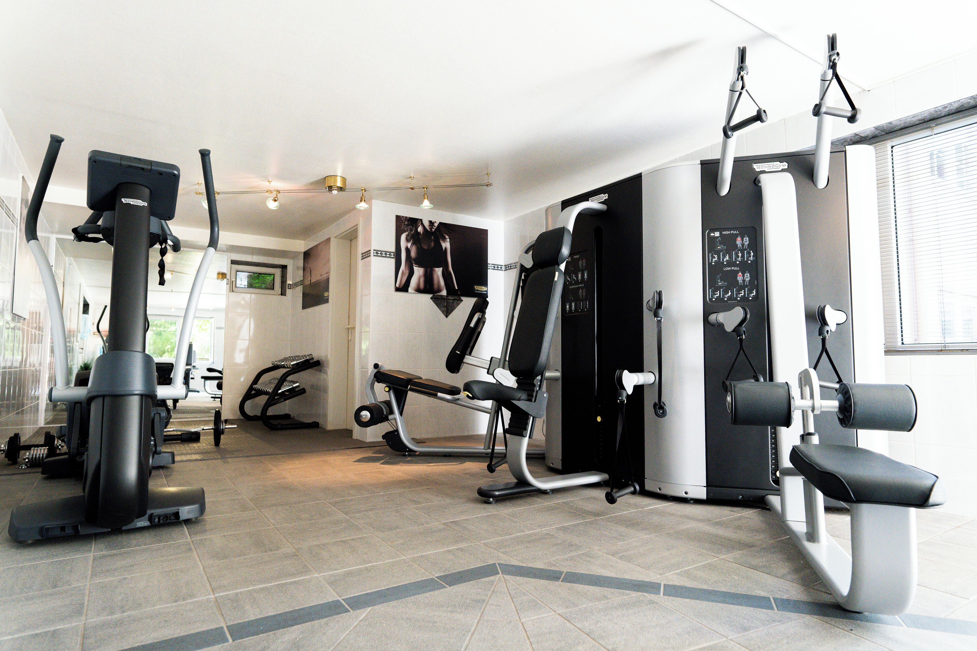 Een sportschool met diverse fitnessapparaten, waaronder een loopband, elliptische trainer en gewichtstoestellen.