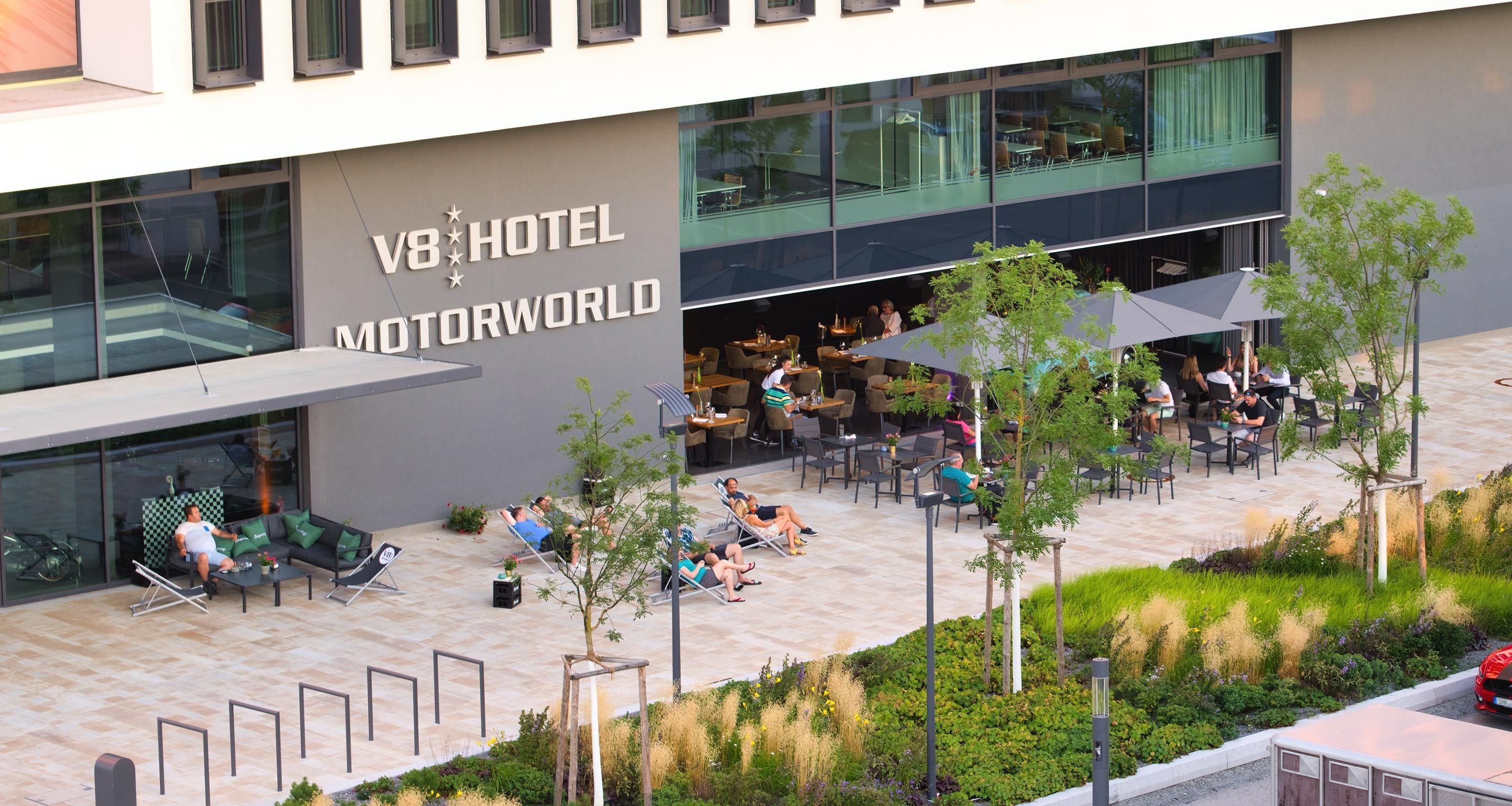 A hotel exterior with outdoor seating and a garden area.
