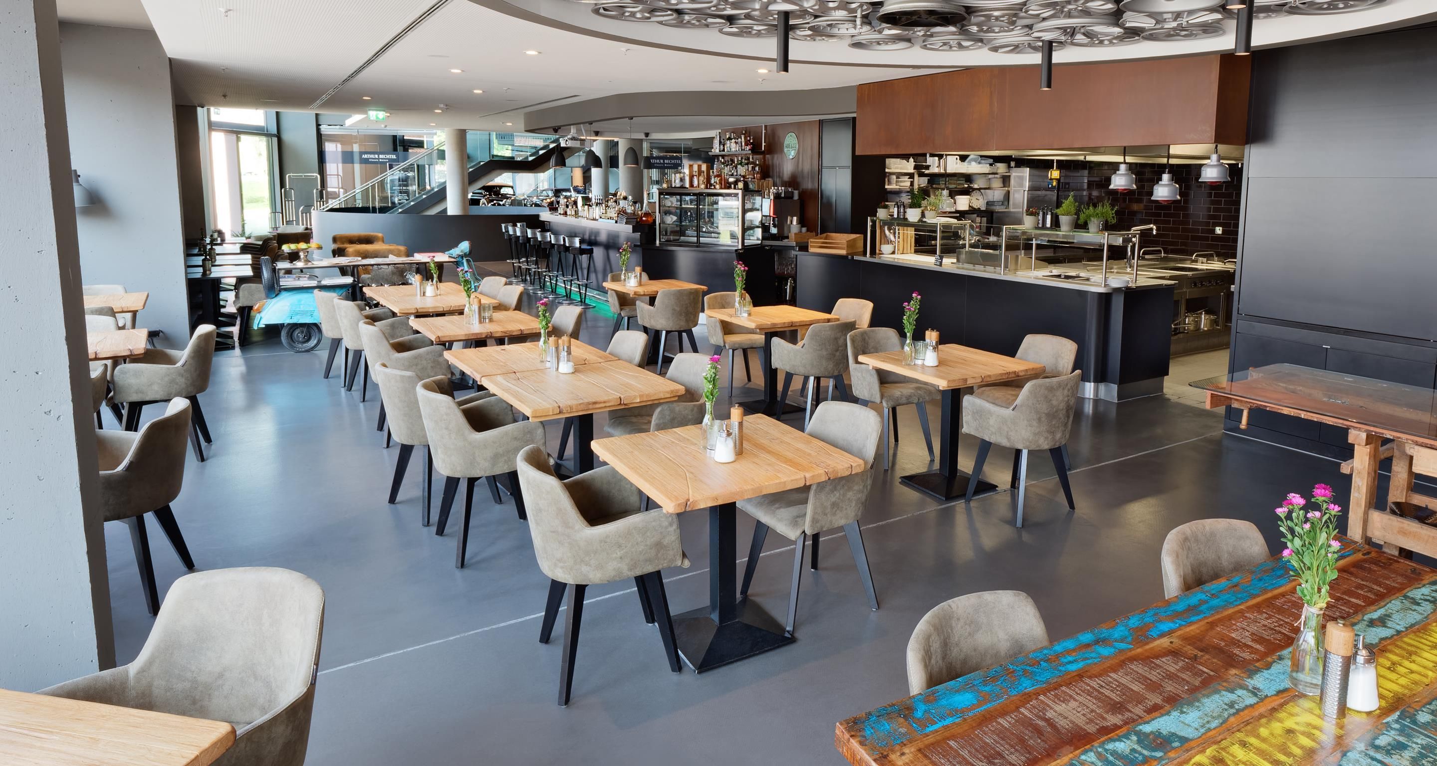 Un restaurante moderno con varias mesas y sillas, una zona de bar y una cocina al fondo.