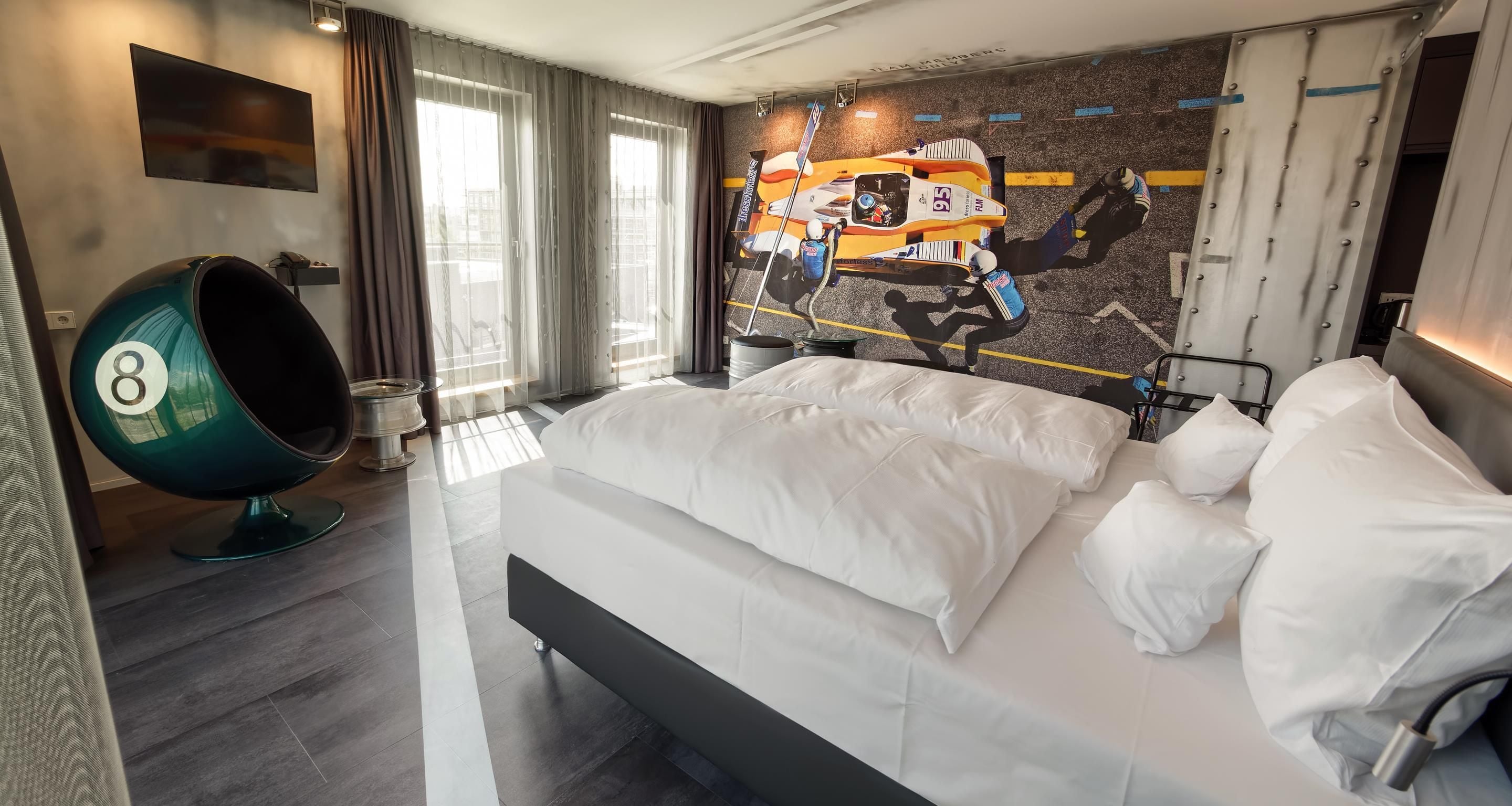 A modern hotel room with a large bed, a unique spherical chair, and a racing car mural on the wall.