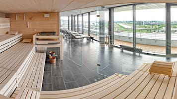 A modern sauna room with wooden benches, a sauna, and a glass wall offering a city view.