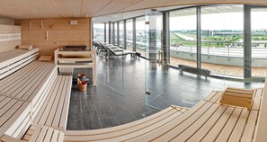A modern sauna room with wooden benches, a sauna, and a glass wall offering a city view. - V8 Hotel Motorworld Region Stuttgart, BW Premier Collection (Boeblingen)