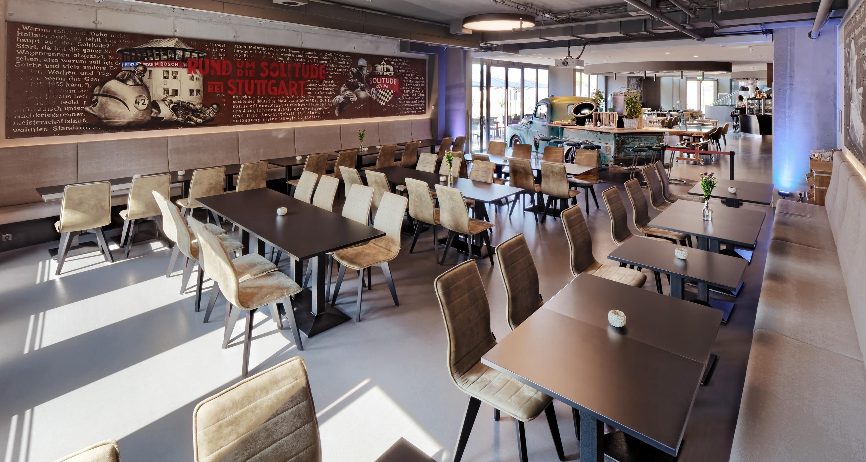 A spacious dining area with multiple tables and chairs, a large mural on the wall, and a bar area in the background.