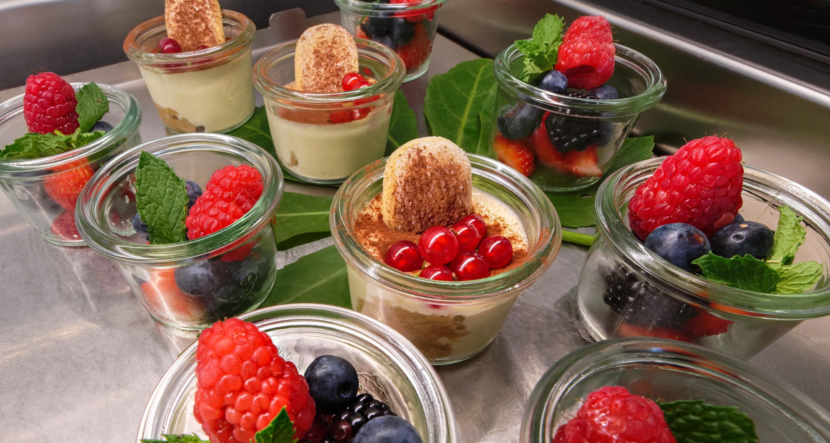 A variety of dessert cups with fruits and a biscuit on a tray.