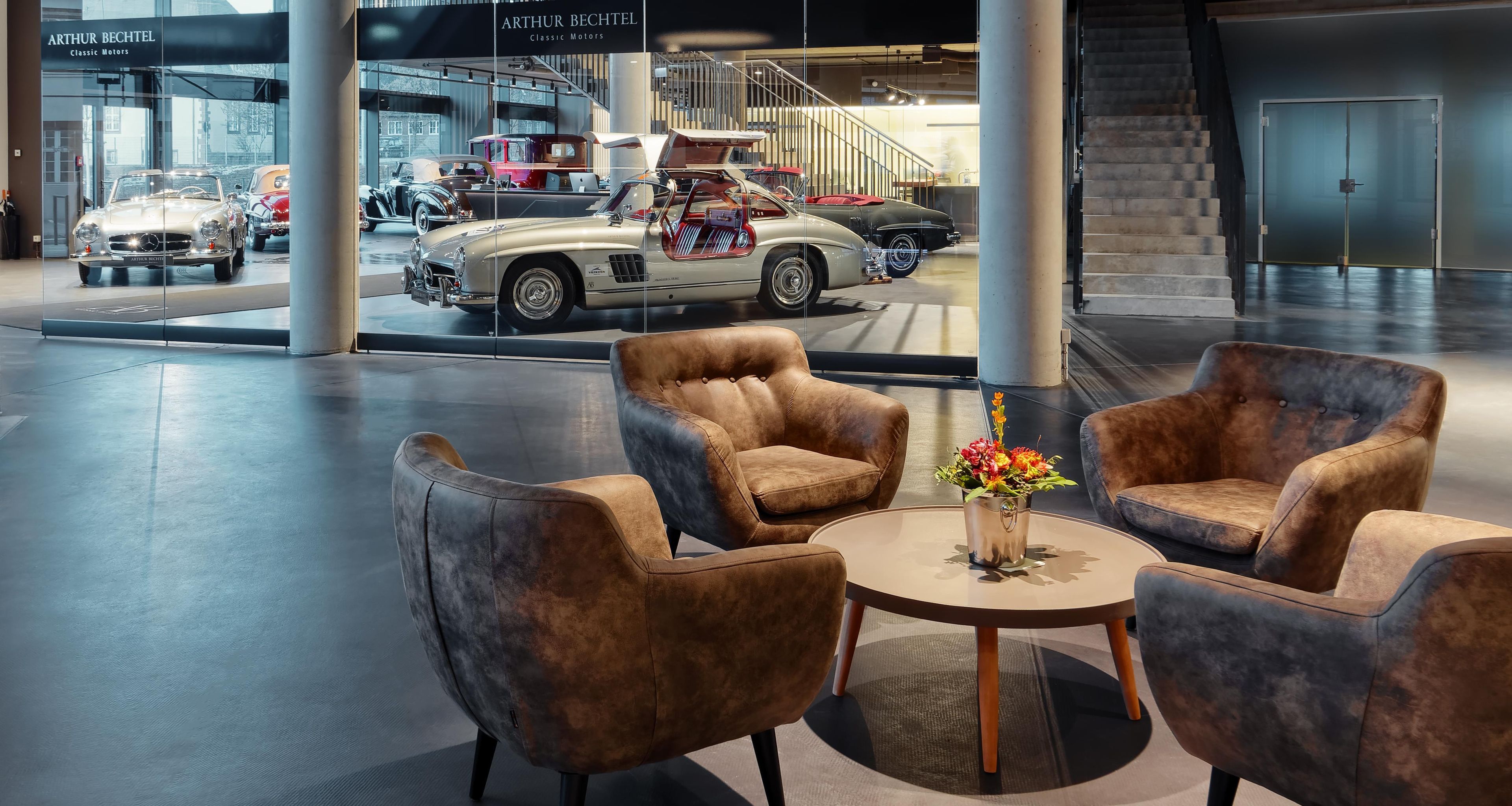 A modern interior with leather armchairs, a round table, and a display of classic cars.