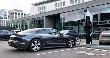 Ein modernes Gebäude mit großen Glasfenstern und einem Parkplatz mit Ladestationen für Elektroautos.