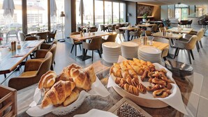 A spacious dining area with multiple tables and chairs, a variety of pastries displayed on tables, and a view of the outside through large windows. - V8 Hotel Motorworld Region Stuttgart, BW Premier Collection (Boeblingen)