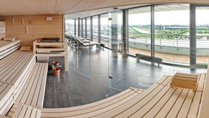 A modern sauna with wooden benches and a glass wall offering a city view. - V8 Hotel Motorworld Region Stuttgart, BW Premier Collection (Boeblingen)