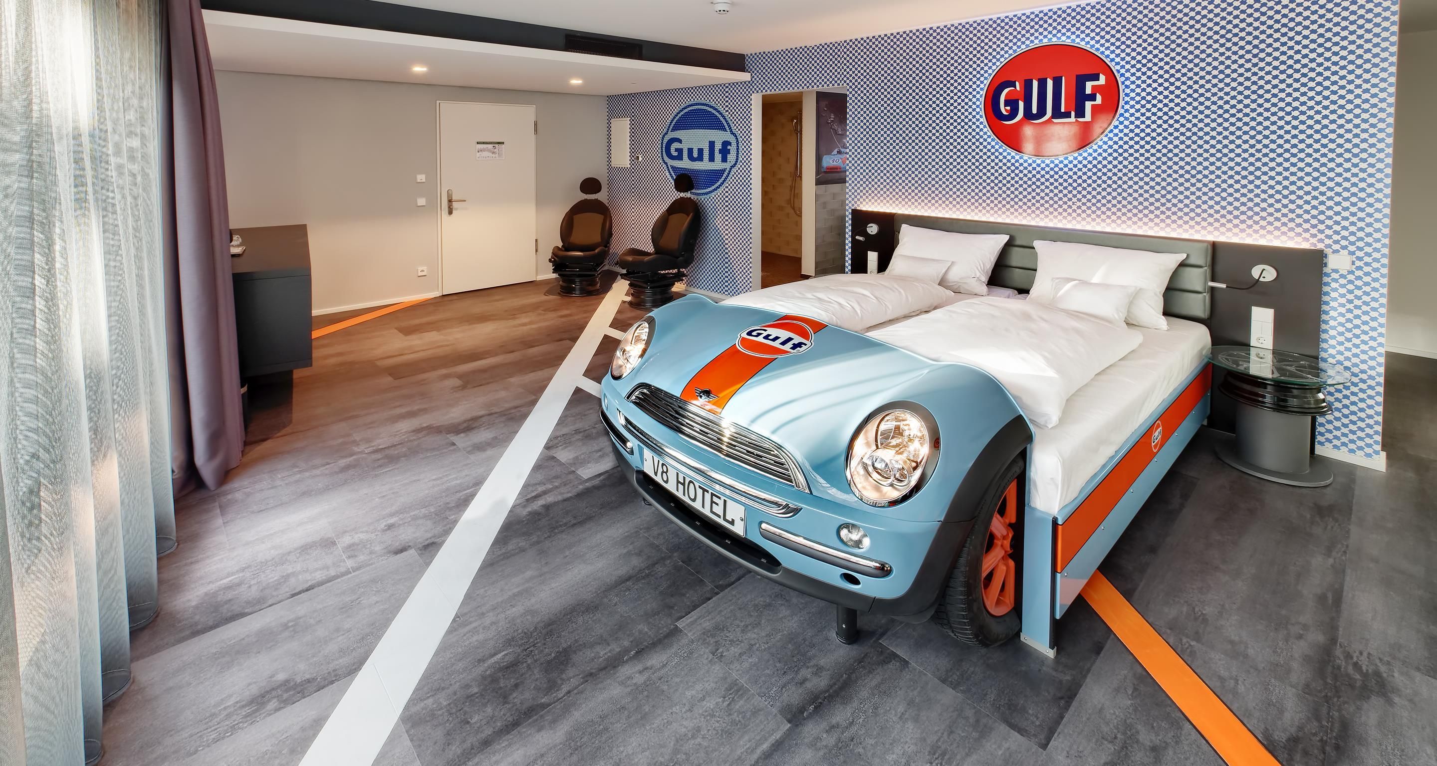 Une chambre avec un lit, un logo Gulf accroché au mur et une maquette de voiture ancienne.