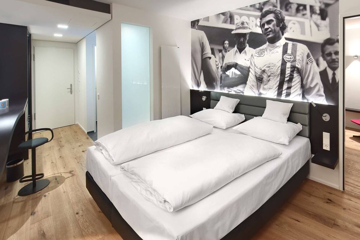 Una habitación de hotel moderna con una cama grande, un escritorio, una silla y un televisor montado en la pared.