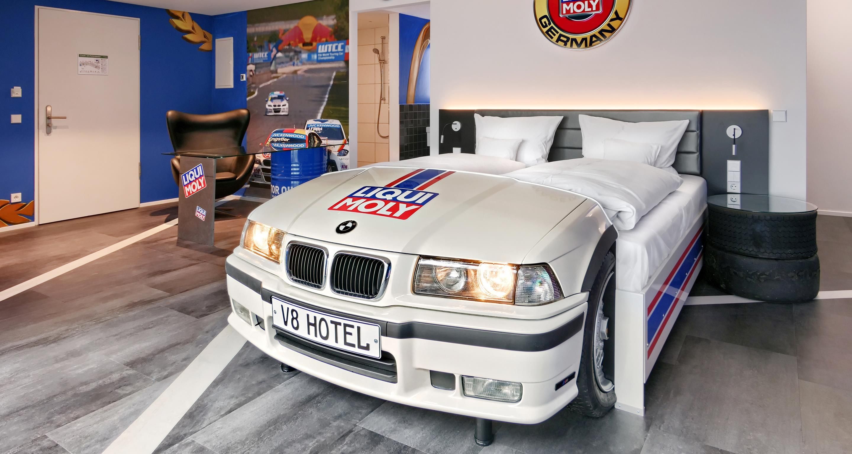 Een kamer met een bed, een BMW automodel en een muur met een logo.