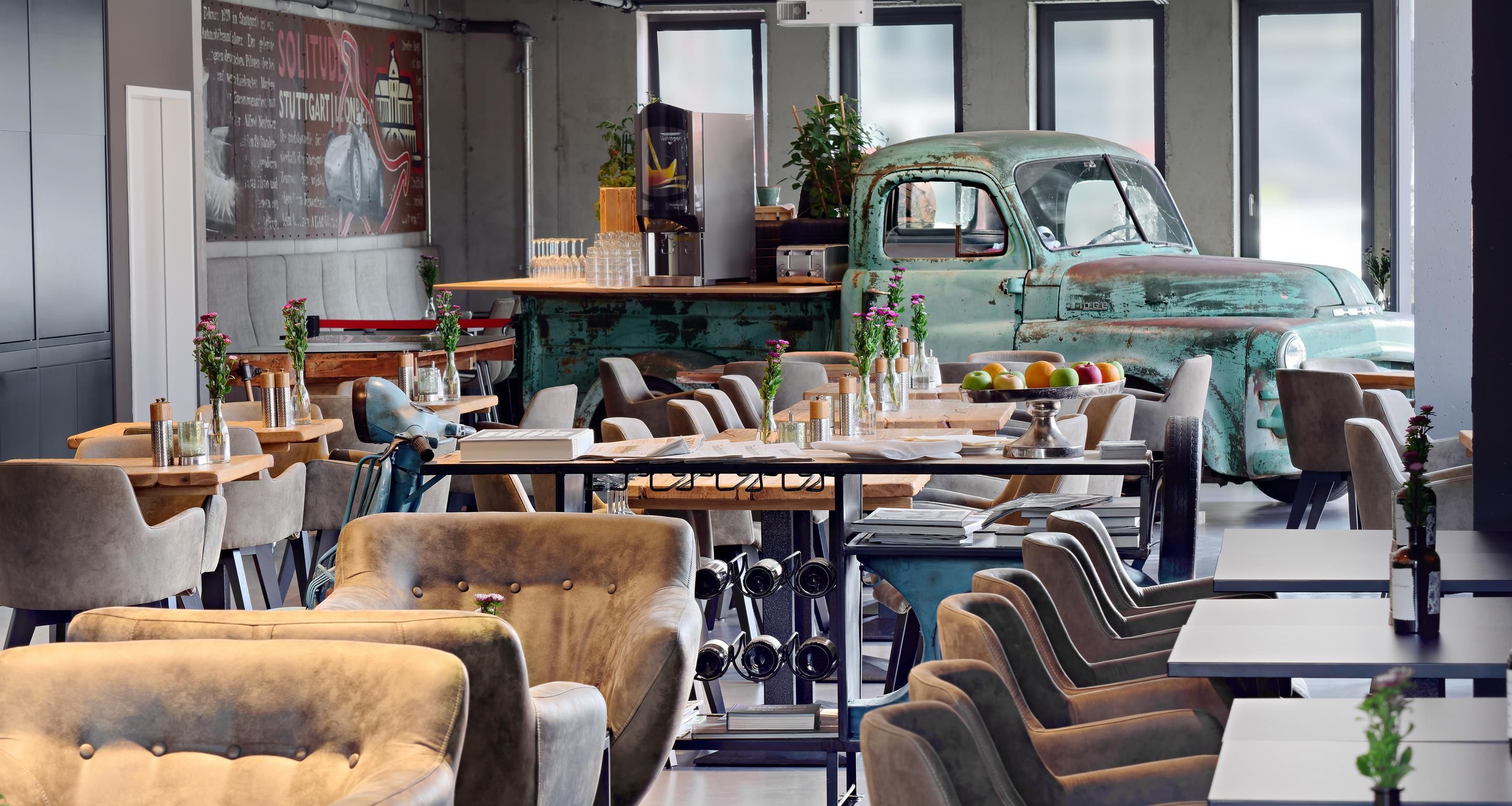 A restaurant with a vintage truck as a centerpiece, modern furniture, and a large poster on the wall.
