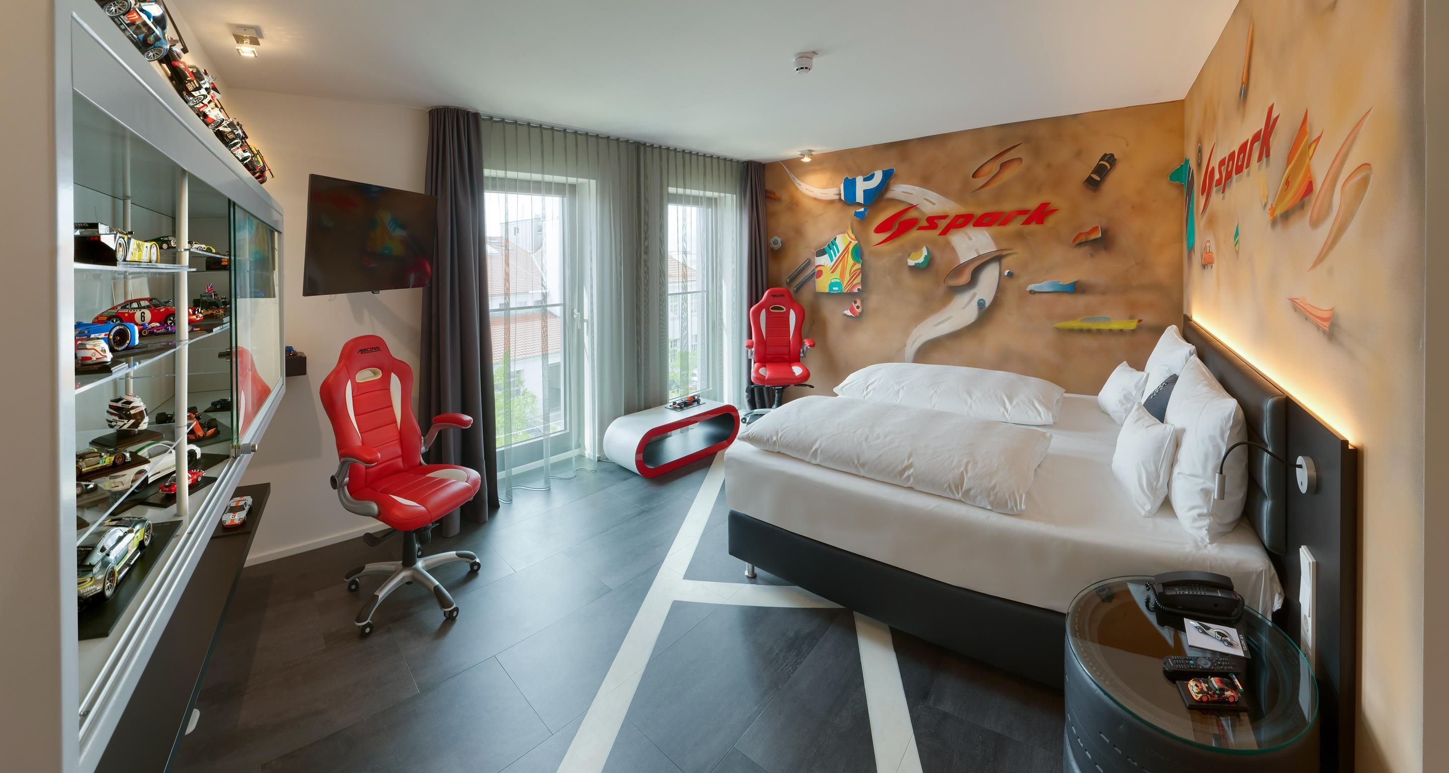 Ein Hotelzimmer mit Bett, Schreibtisch, Stuhl, Fernseher und einer Wand mit Kletterwand-Motiv.