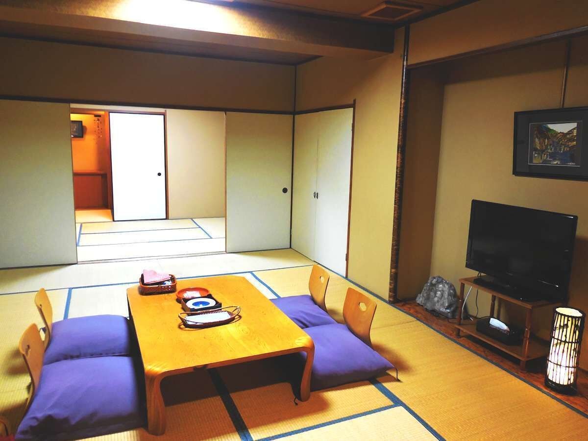 A traditional Japanese room with tatami flooring, a low wooden table with cushions, a television on a stand, and a sliding door leading to another room.