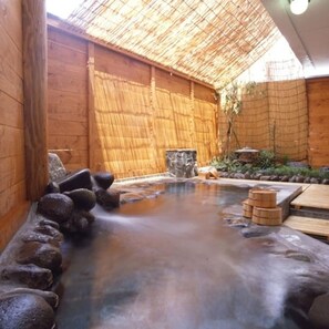 Un área de aguas termales con paredes de madera, una balsa de piedra y escalones de madera que bajan al agua.
