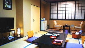 A traditional Japanese-style room with tatami flooring, a low table with cushions, a television, and a sliding door.
