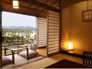 A traditional Japanese room with tatami flooring, a low table, a chair, and a view of a natural landscape.