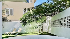 Zona de piscina exterior con sillas de descanso y un árbol que da sombra.
