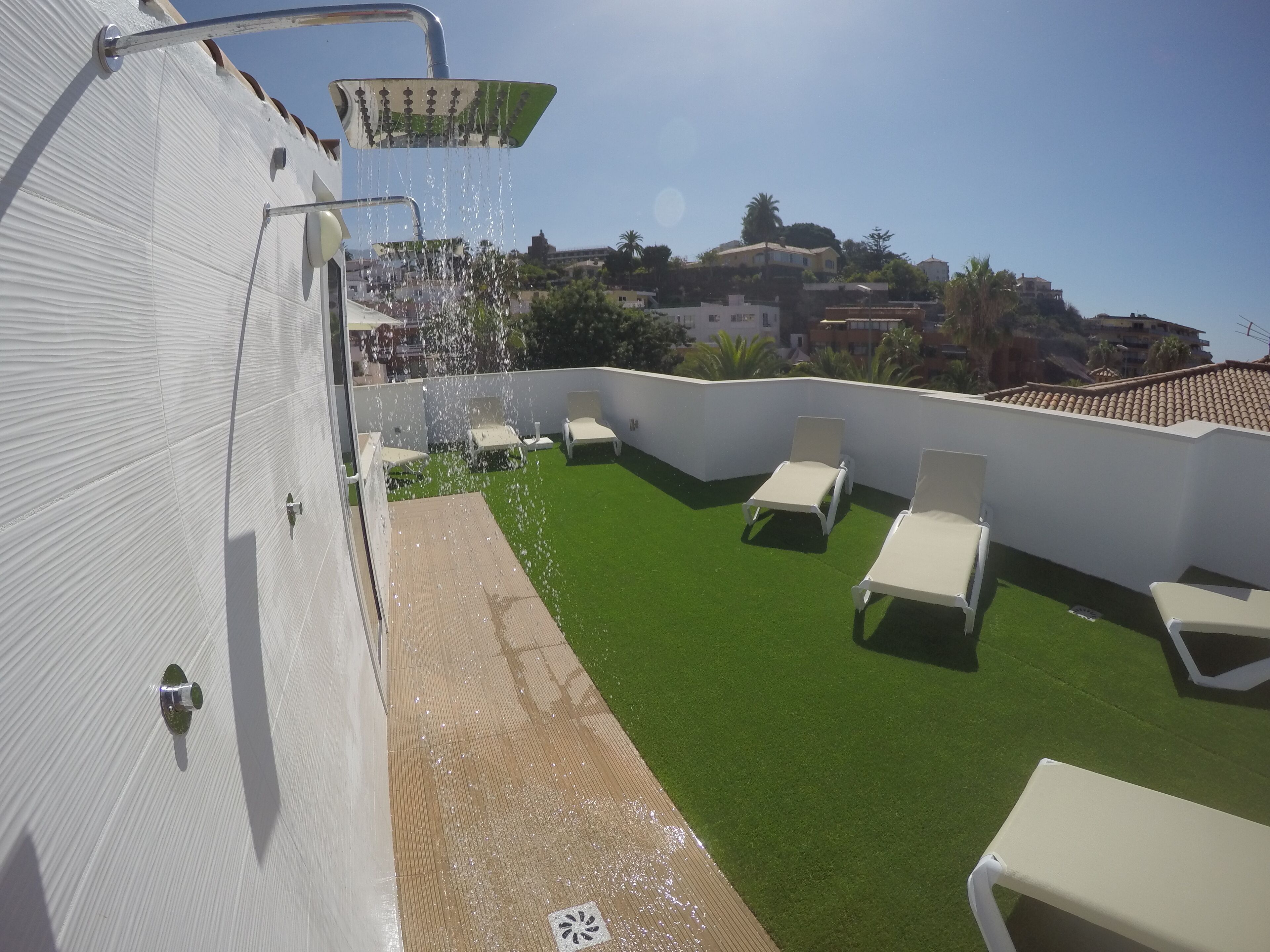 A rooftop terrace with artificial grass, white lounge chairs, and a water feature.