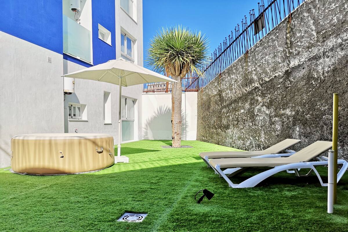 A pool area with a hot tub, lounge chairs, and a palm tree.
