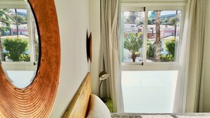 Un dormitorio con un ventanal grande, cabecera de madera, un espejo y una colcha estampada.