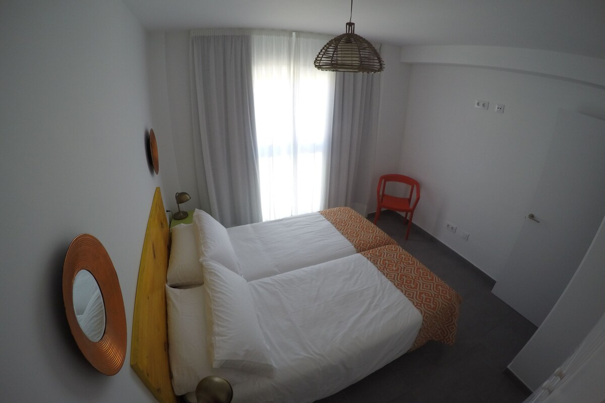 A hotel room with a large bed, a chair, a desk with a lamp, and a window with curtains.