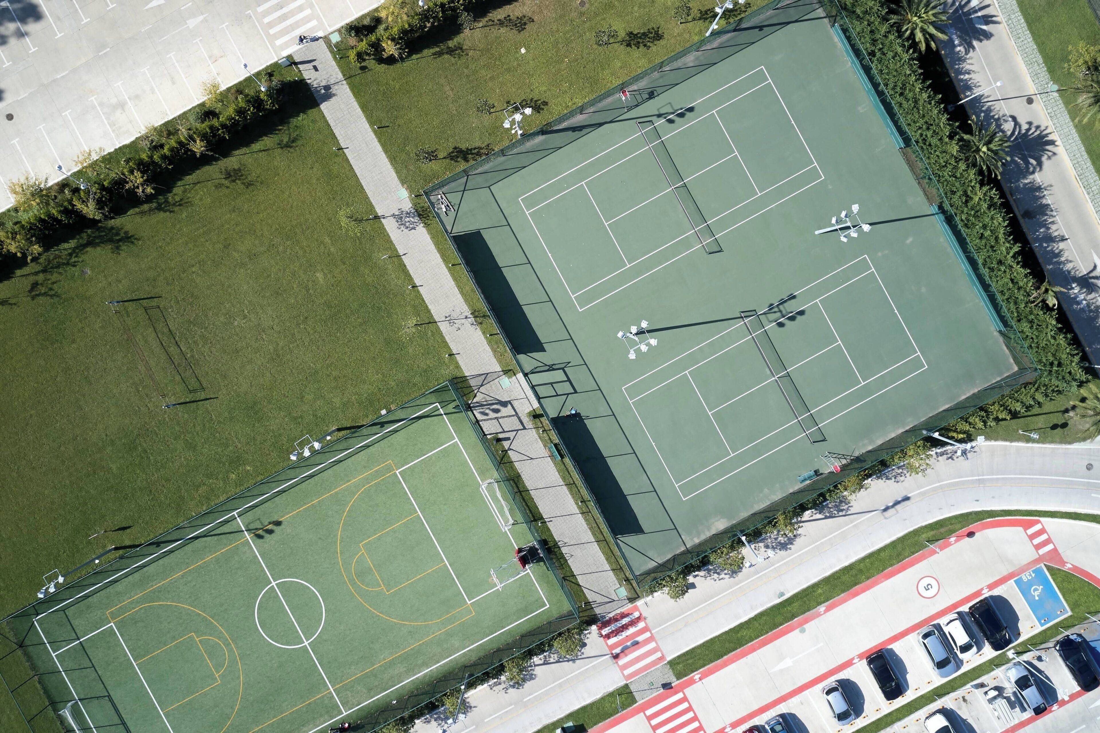 An aerial view of a sports complex with multiple tennis courts, parking areas, and surrounding greenery.