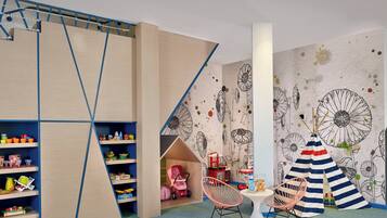 A children's playroom with a climbing wall, shelves with toys, a teepee, and a mural with dandelion patterns.