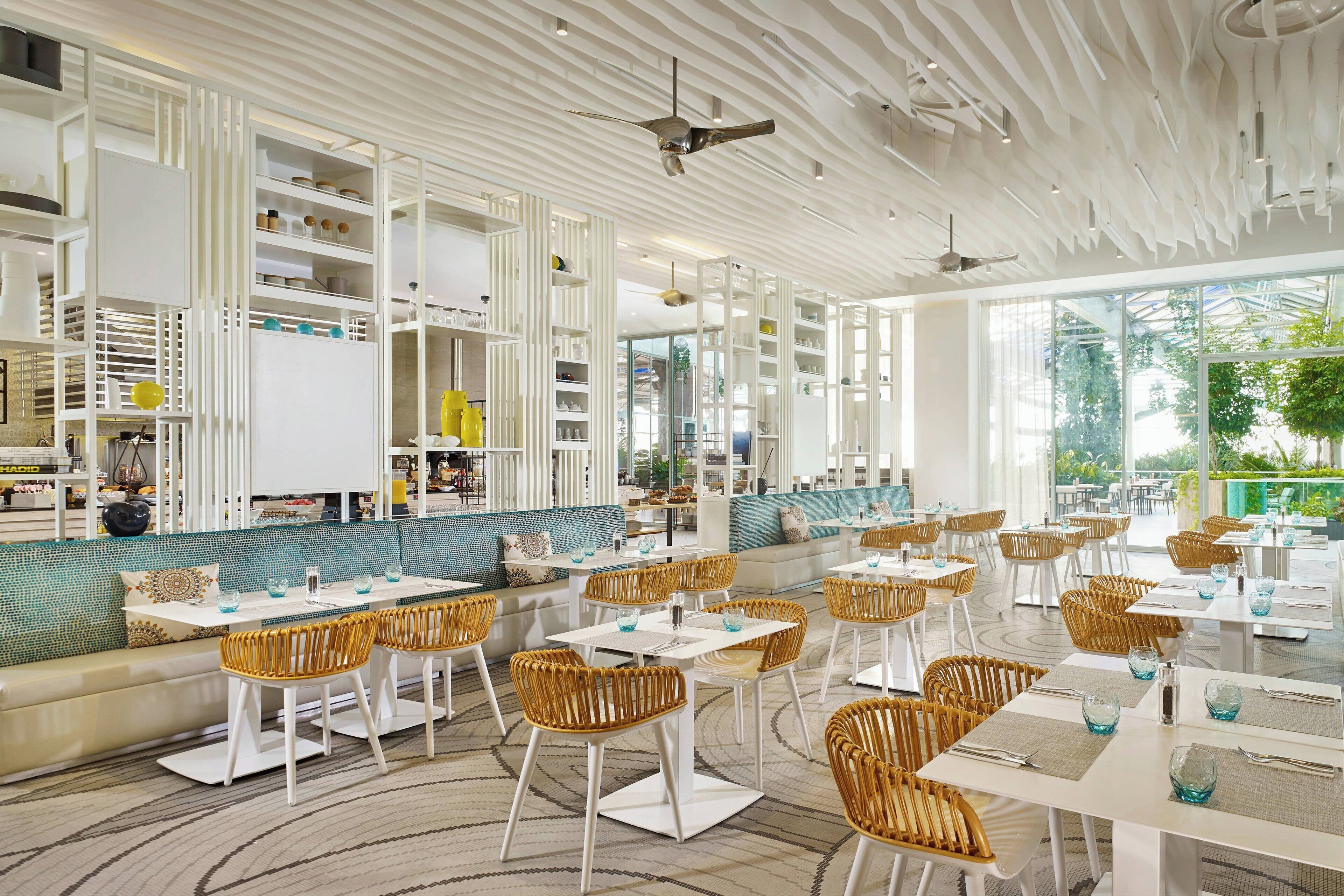 A modern restaurant with white furniture, a patterned ceiling, and large windows offering a view of the outdoors.