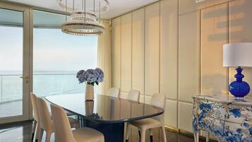 A modern dining area with a glass table, white chairs, and a view of the sea.