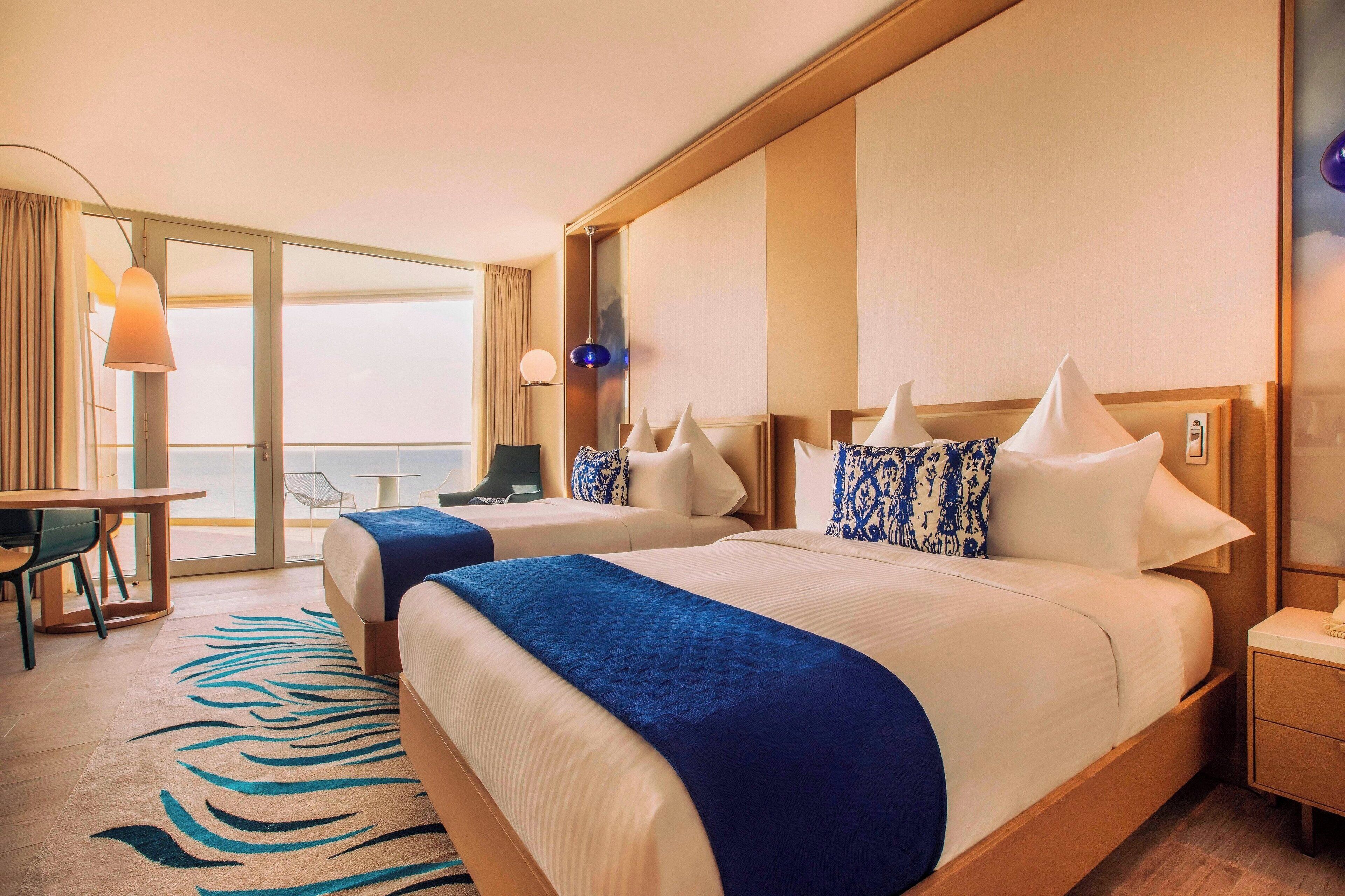 Habitación de hotel con dos camas, un escritorio y vista al océano.