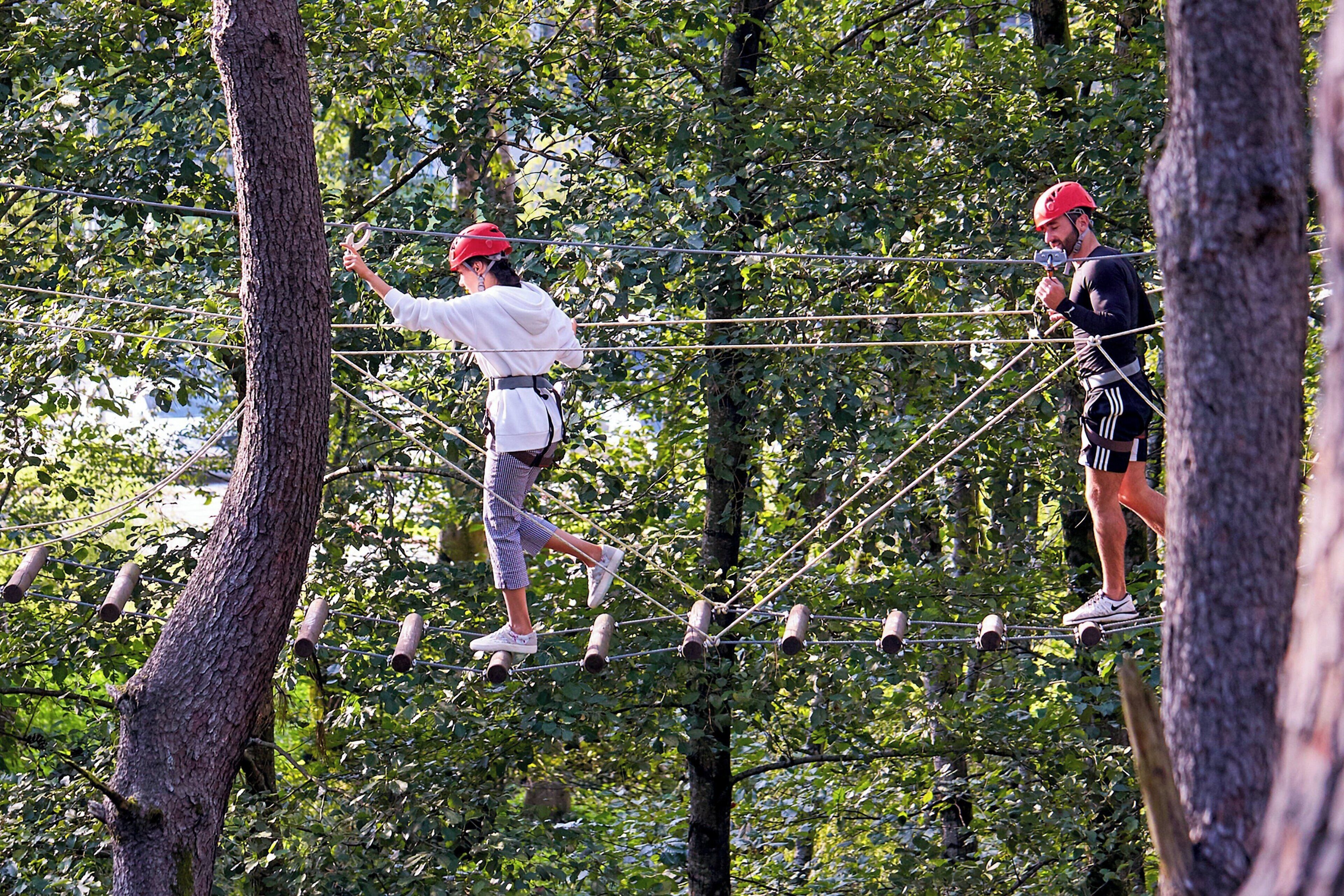 Two people navigating a rope bridge in a wooded area.