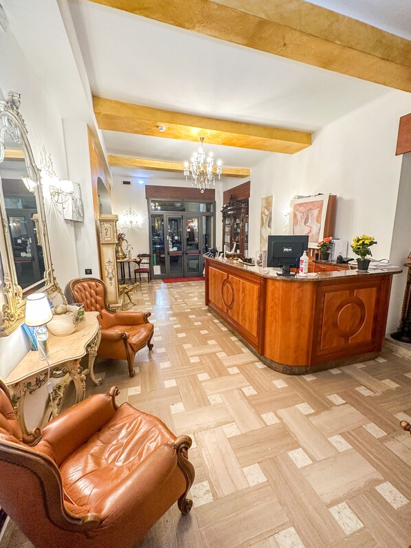 A spacious living area with a wooden floor, leather chairs, a wooden coffee table, a chandelier, and a large mirror.