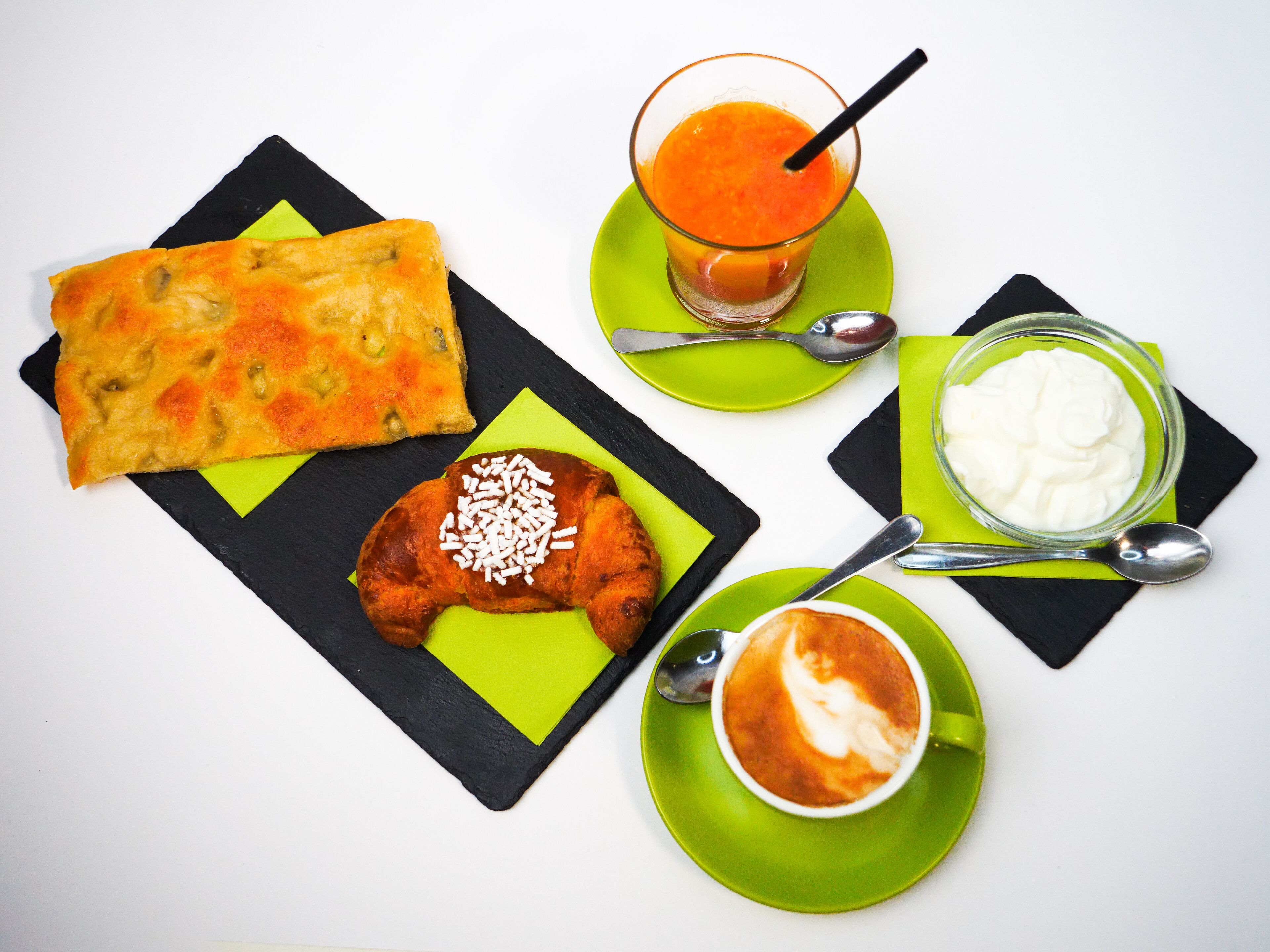 Ein Frühstücksbuffet mit einem Croissant, einer Scheibe Brot, einem Glas Orangensaft, einer Schale Joghurt und einer Tasse Kaffee.