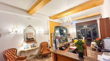 Een hotellobby met een receptiebalie, een grote spiegel, een kroonluchter en een zithoek met lederen fauteuils.