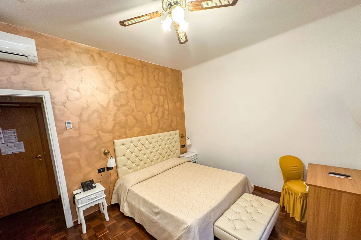 Un dormitorio con cama, mesita de noche, silla, escritorio y equipo de aire acondicionado.