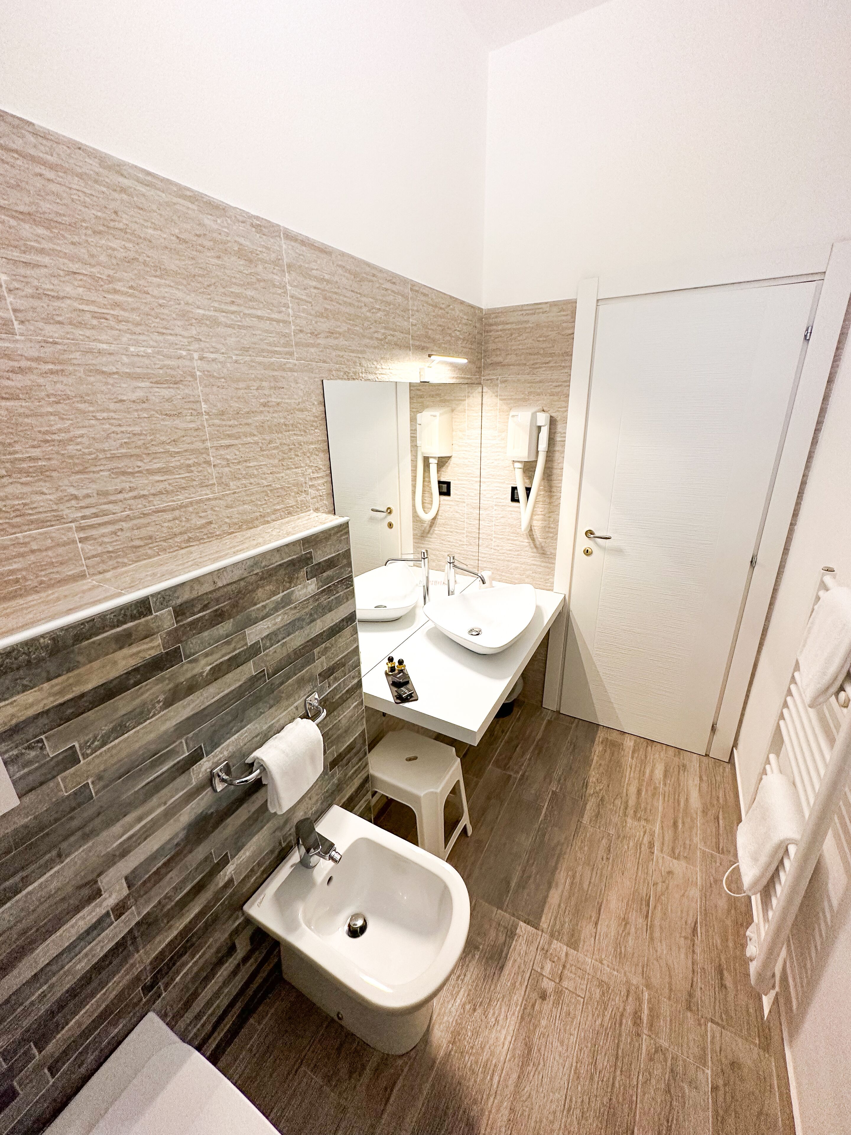 A modern bathroom with a bidet, two sinks, a mirror, and a towel rack.