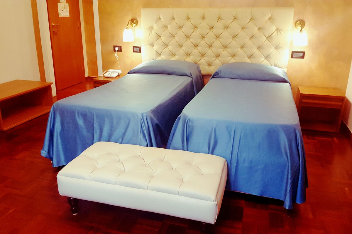 Une chambre d’hôtel avec deux lits, un banc et des lampes de chevet.