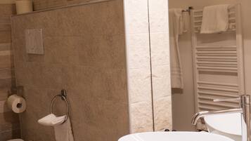 Une salle de bain moderne avec un mur recouvert de carreaux beiges, un grand lavabo blanc, un bidet et un porte-serviettes.