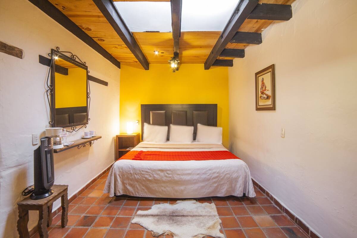 Un dormitorio con cama, mesita de noche, espejo, calefactor y alfombra.