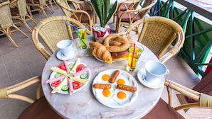 Una mesa servida con desayuno, incluyendo huevos, salchichas, croissants y una variedad de verduras frescas.