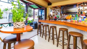Una zona de bar con taburetes, un televisor y una variedad de botellas y vasos en estantes.