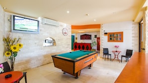 Una mesa de billar en una sala con un reloj, un televisor y una zona de bar.